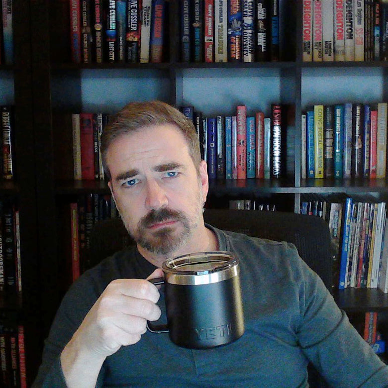 The author, Benjamin Wallace, sitting in front of a bookcase with a cup of coffee